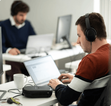 Two Employees Focused Working on Laptops at Desks Wearing Headphones -FundedNext